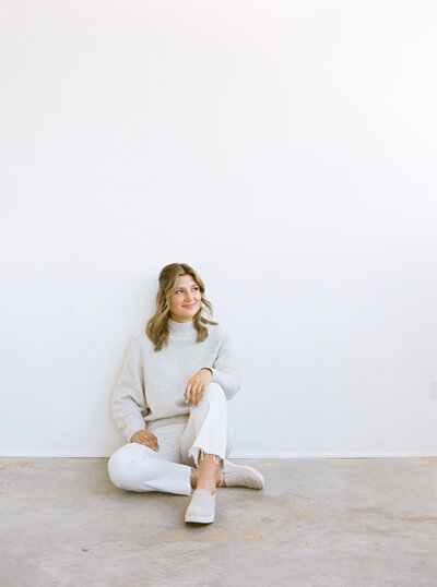 Brand photographer in Denver featuring client sitting down leaning up across a white wall.
