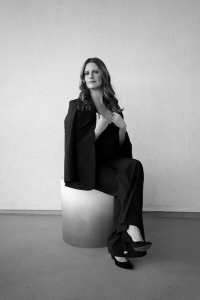 Chic dressed wedding planner on a stool with jacket over her shoulders