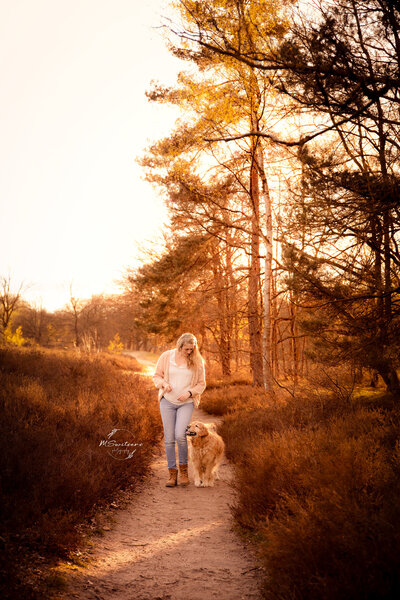 Dogmom op wandel met haar golden retriever in de heide tijdens zonsondergang.