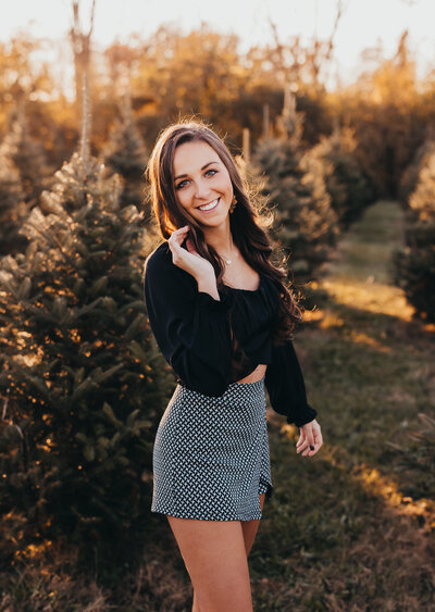 Portrait of woman posing in front of evergreen trees during golden hour