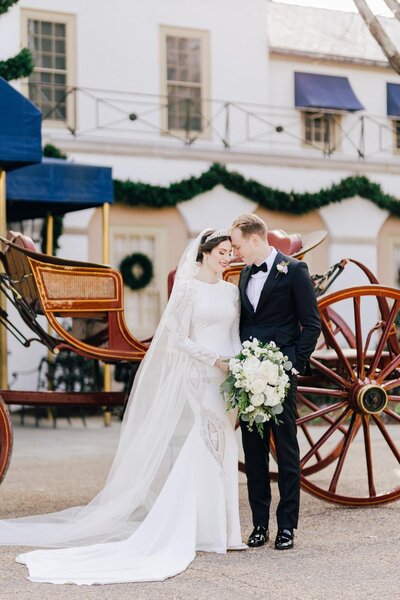A bride and groom stand in front of a carriage at the Williamsburg Inn.