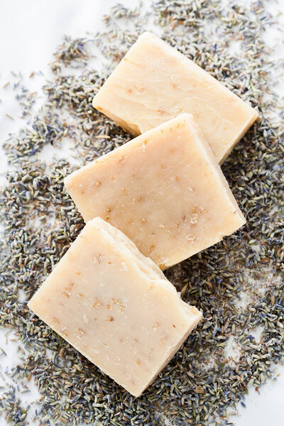 Three rectangular bars of handmade soap rest on dried lavender buds, arranged against a white background—an ideal scene for branding photography Jacksonville, with the soap’s natural texture and oatmeal flakes captured in crisp detail.