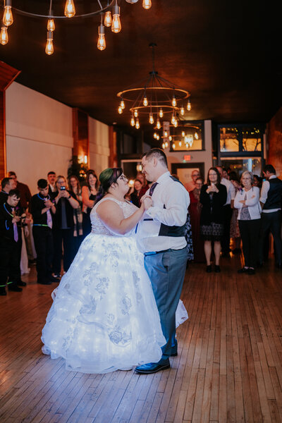 Bride and groom share their first dance under glowing Edison lights, captured by a wedding photographer in Minnesota during a cozy indoor reception.