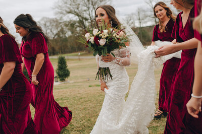 Bridesmaids hold up brides train while walking