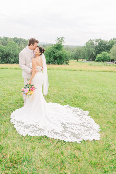 A laughing brunette bride getting kisses on her temple by her husband in the Blue Ridge mountains while enjoying their destination wedding photos by JoLynn Photography