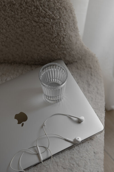 A laptop, a glass of water and headphones on top of an armchair