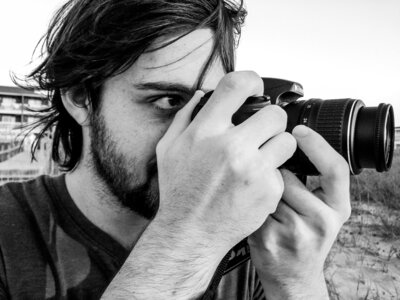 An old photo in black and white of a younger Reg holding his camera close to his face and shooting something off to the right.