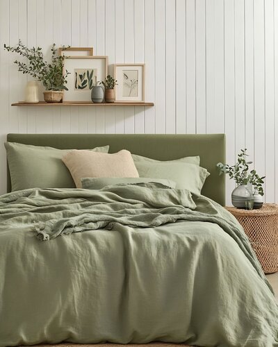 Sage green bedroom featuring layered bedding, natural textures, and minimalist wall art.