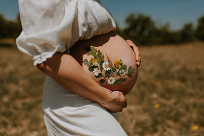 A Pregnant Mom holding her bare belly with dried florals stuck on it in a field in fort worth, tx