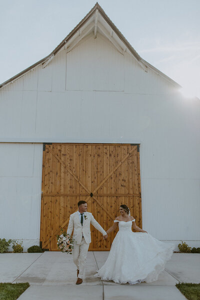 bride and groom hold hands in front of barn wedding venue