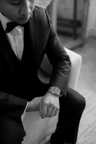 Groom adjusting luxury wristwatch while seated in suit at Tree House Venue in Vero Beach, Florida, captured during intimate wedding day preparations.