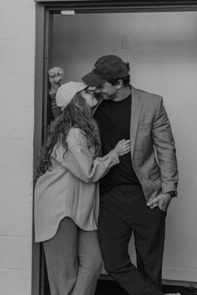 Big Sur Downtown Elopement Session. Couple in baseball caps and blazers leaning in for a kiss outside coffee shop