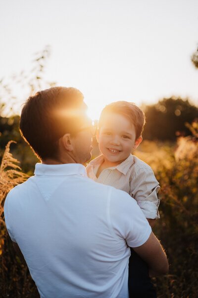 Vater hält lächelnden Sohn auf dem Arm während Golden Hour