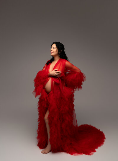Red tulle maternity robe with dramatic ruffles and train worn open in a studio setting