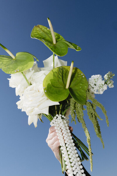An editorial shot of a bouquet-- with green & white flowers with strands of pearls dangling