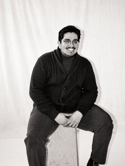 Black and white film portrait of Javi, seated and smiling at the camera — co-founder and cinematographer at Castillo Holliday Photo + Film.