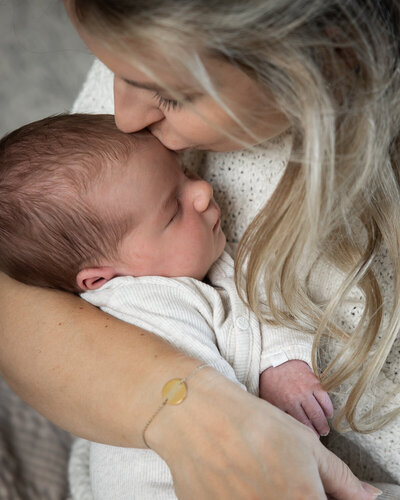Een moeder heeft haar newborn in haar handen en geeft haar een kus tijdens een fotoshoot