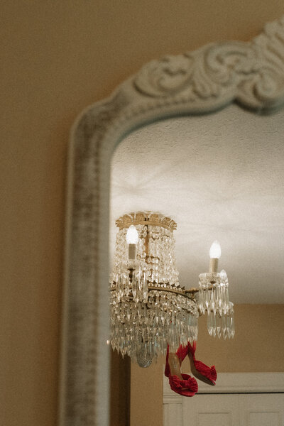 Artistic reflection of a chandelier and red heels captured in a vintage mirror, photographed by Rainstorm Photo & Video with cinematic, editorial detail.