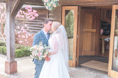 Bride and groom kissing outside the entrance to Sandhole Oak Wedding Barn in Cheshire