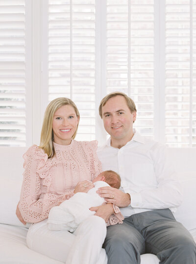 mother and father holding newborn baby  sitting on a couch