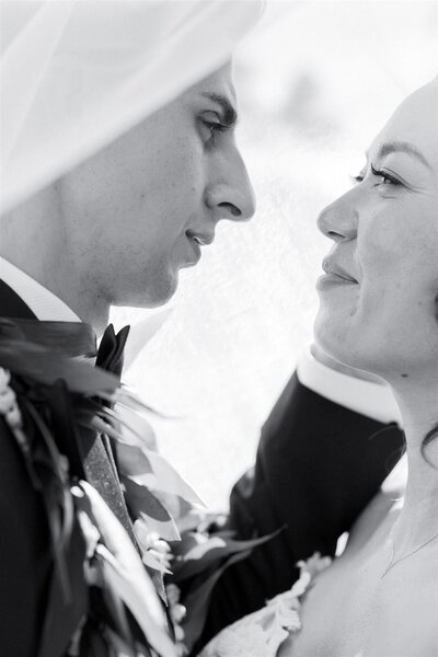 A newlywed couple looking at each other intimately while under a veil 
