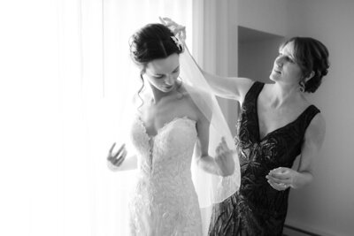 black and white portrait of a bride putting her veil on