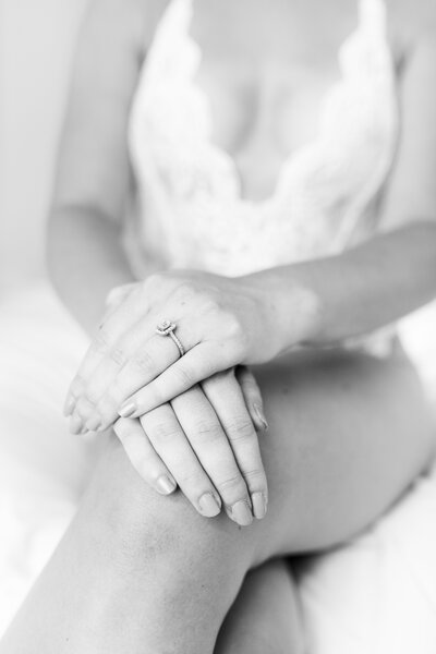 Hand with engagement ring are folded over knee as woman sits on bed during Minneapolis boudoir photoshoot.