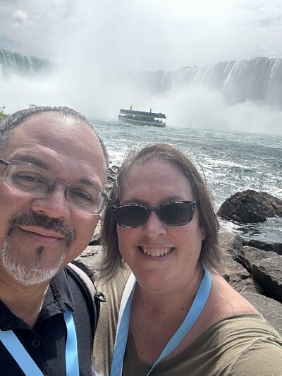 A man and a woman are in front of Niagara Falls  with a boat in the background.