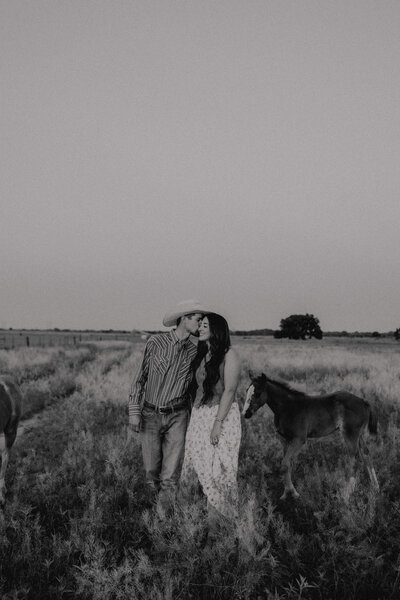 groom kisses bride on the cheek walking through field at oklahoma couples session