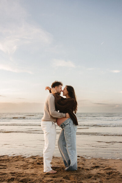 Zwangerschapsshoot op het strand van Katwijk met een koppel dat elkaar omhelst tijdens zonsondergang.