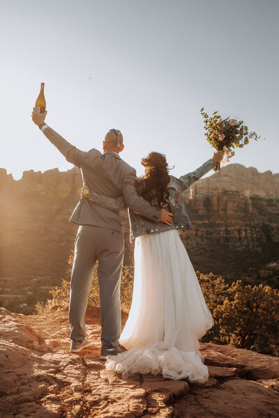 wedding couple celebrating in sedona in a denim jacket with champagne amd succulent florals