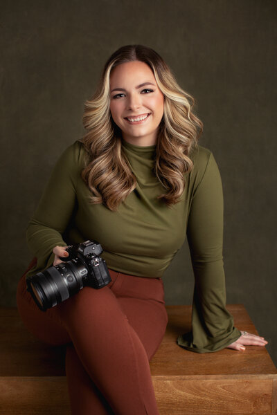 The owner of Kara Reese Photography, Kara Krause, pictured holding her camera for a headshot.