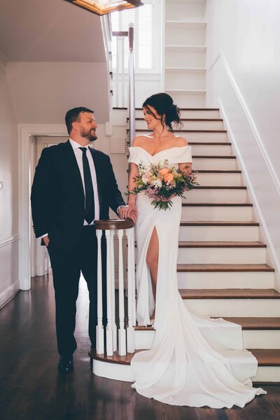 Destination wedding photography by Britt Elizabeth captures couple holding hands looking at each other on a white staircase.