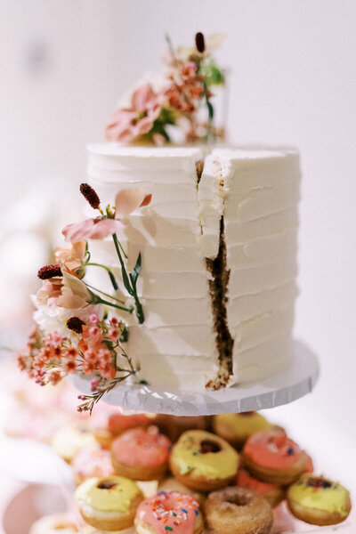 White buttercream cake decorated with fresh flowers, surrounded by donuts at Oakville wedding reception