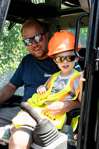 Ryan Kornelsen with small son sitting on his lap operating equipment during a pond build