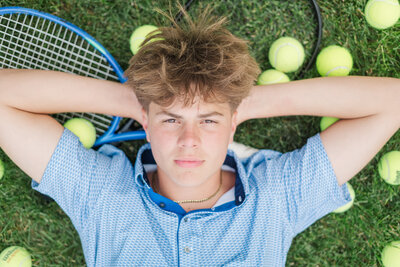 a guy laying in the grass with a tennis racket surrounded by tennis balls