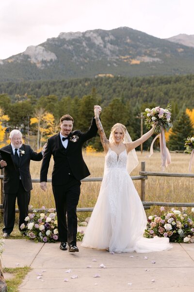 Bride and groom celebrating their wedding ceremony with mountain views in Colorado, walking down the aisle with florals lining the path at Wild Basin Lodge