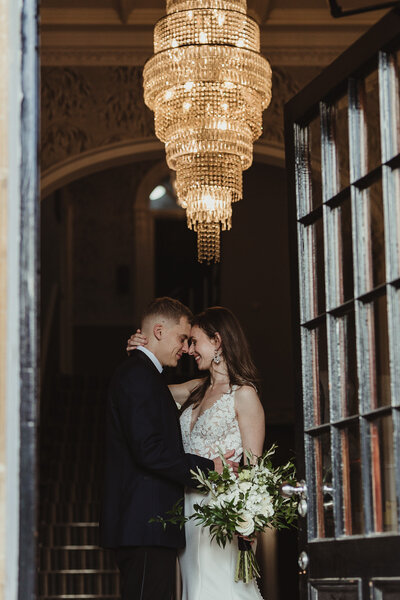 couple standing under chandelier wedding portrait