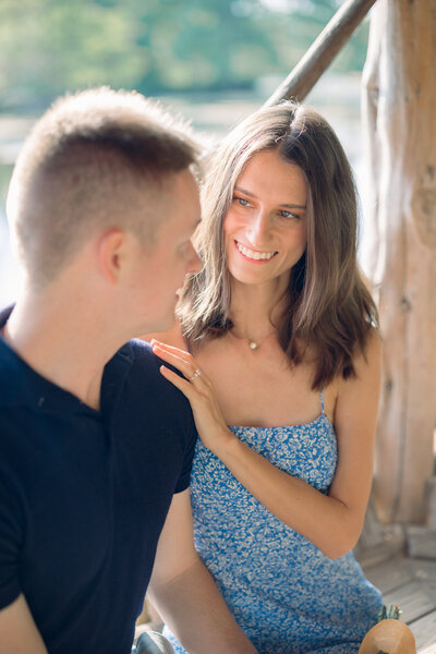 Bride-to-be in a blue floral dress smiling at her fiancé during a golden hour engagement session at Landa Park in New Braunfels, Texas.