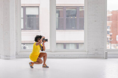 african american chicago photographer wearing yellow dressing holding camera to her face