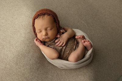 A curious toddler and a relaxed dog peek over the edge of a sofa, watching over a newborn baby, masterfully captured by a Harrisburg newborn photographer, swaddled in a red blanket resting on