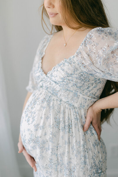 knoxville maternity photographer mom in blue and white dress holding baby bump while looking out window
