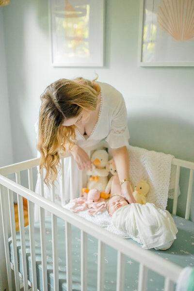 In-home lifestyle newborn session by Oak and Lore Studio, where a mother leans over her newborn baby in a crib in the nursery. The mother looks at her baby with love and tenderness, capturing a quiet, intimate moment in a beautifully styled nursery