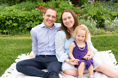 Family of three sits on a blanket together during their family photo shoot at Arneson Acres Park in Edina, MN.