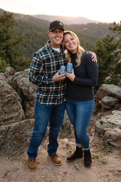 Couple celebrating their engagement on a mountain overlook in Breckenridge — cracking open beers together while stunning peaks and a vibrant sunset create a breathtaking backdrop. Captured with authenticity and creativity, true-to-color editing highlights their genuine connection.