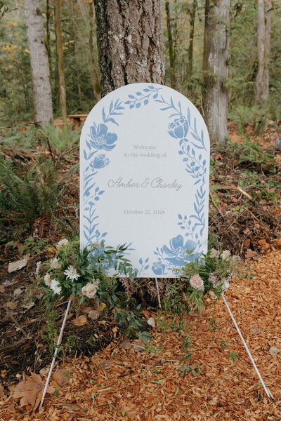 Floral wedding welcome sign for Amber & Charley among forest trees