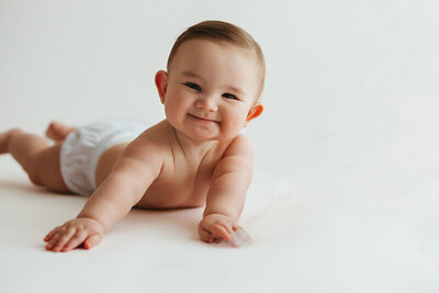 six month old baby boy laying on his belly smiling at the camera with no shirt on or his milestone session