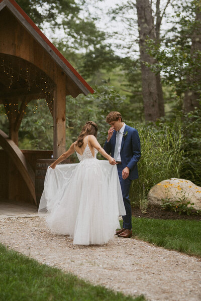 Bride in a wedding dress showing the layers of her dress to the groom in a blue suit during their first look at the Old Saco Inn and Bistro in Fryeburg, Maine.