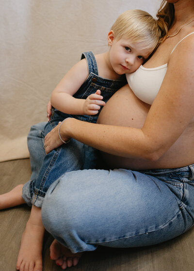 Mother holding her young son against her pregnant belly during a relaxed in-home maternity session in Monrovia, California