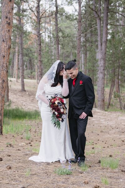 A bride whispers something into the groom's ear as they stand side by side.